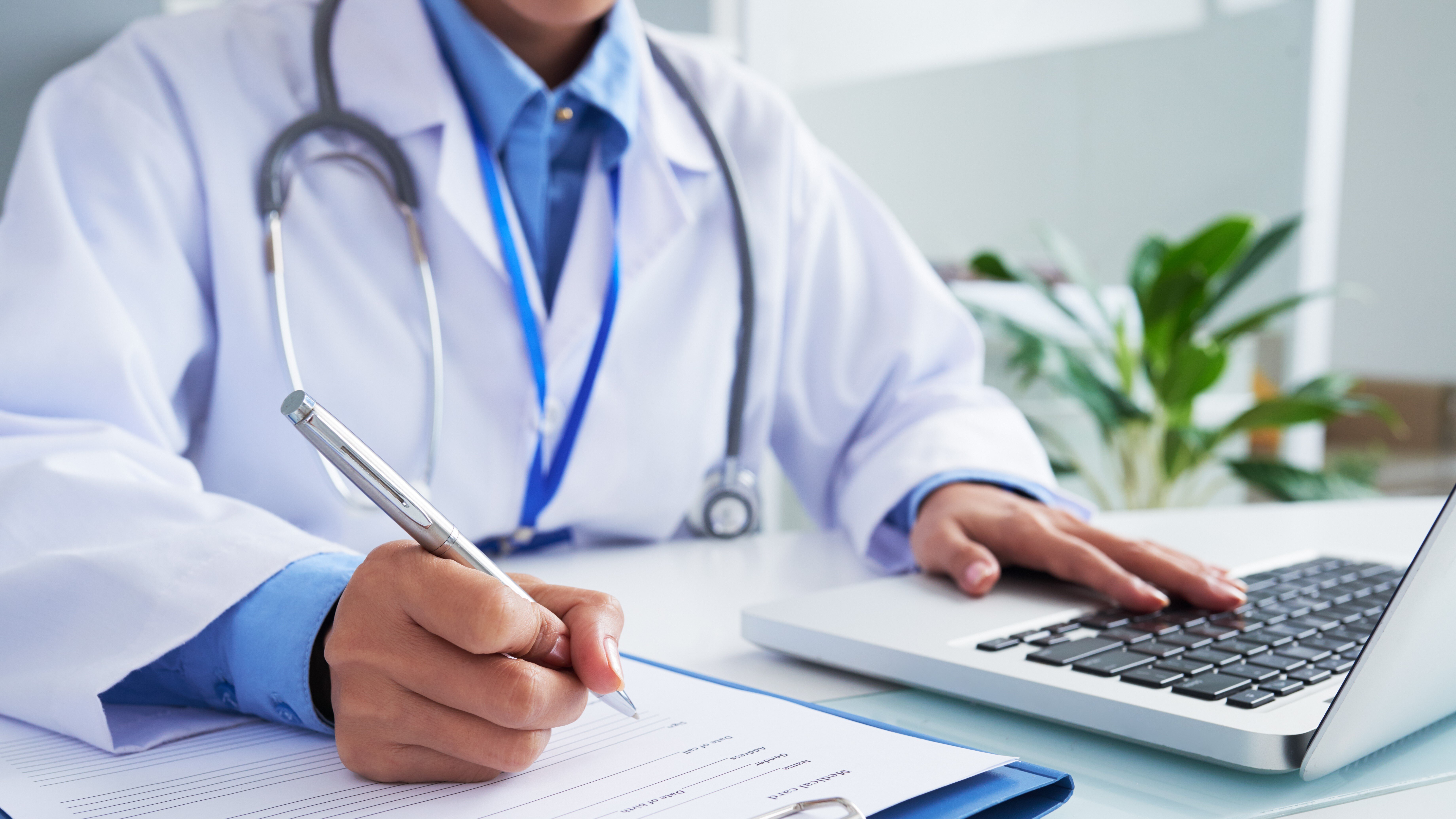 Physician wearing a stethoscope writing on a paper pad